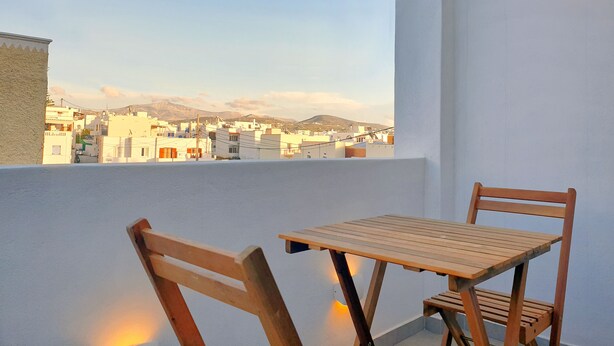 A balcony with a wooden table and chairs, overlooking a cityscape with buildings and mountains. - Modern 2bedroom apartment in the heart of Naxos, walking distance to the beach (Naxos)