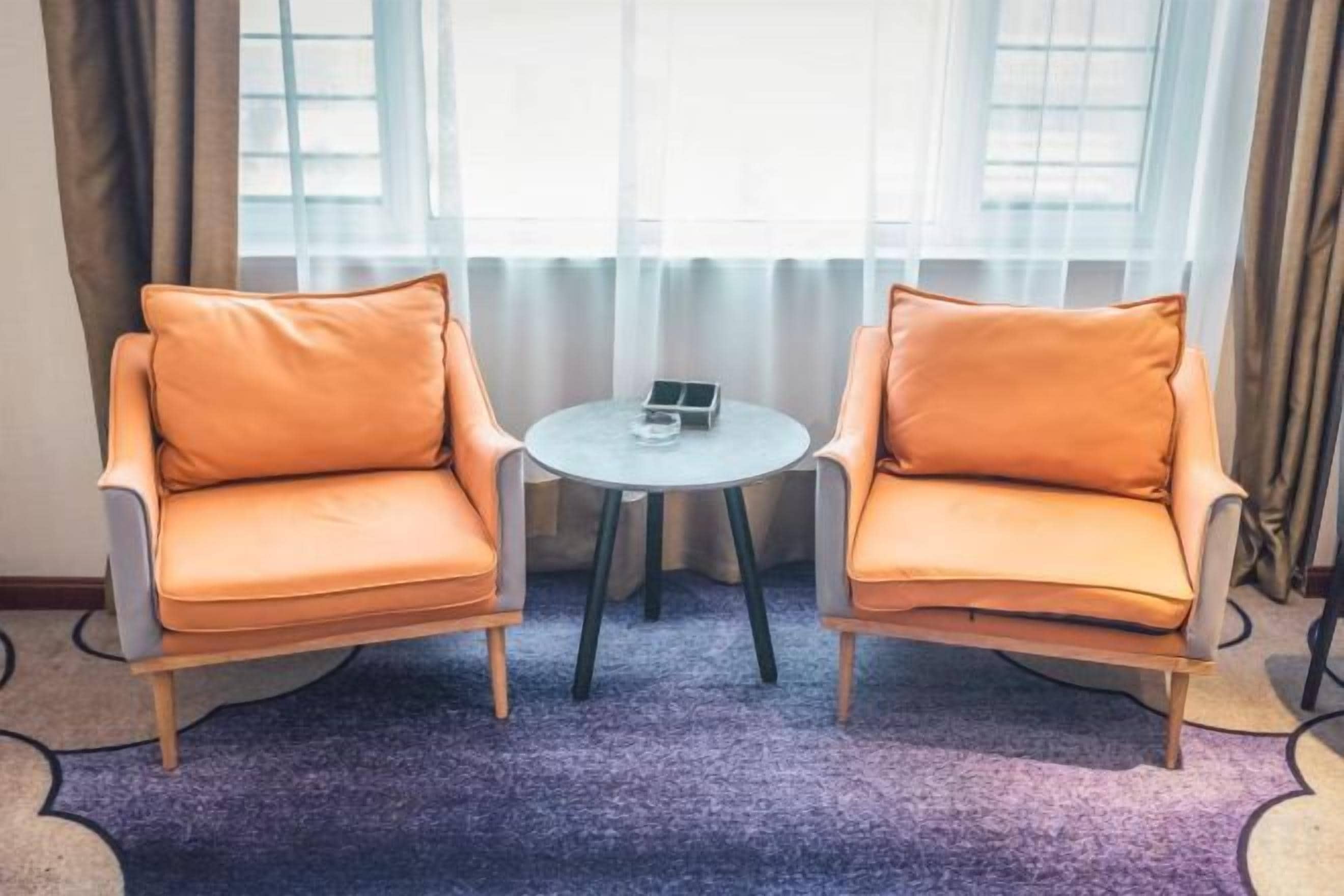 Two armchairs with a small table between them, a window with curtains, and a purple carpet.