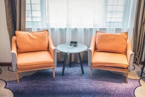 Dos sillones con una mesita entre ellos, una ventana con cortinas y una alfombra morada.