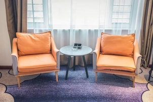 Dos sillones con una mesita entre ellos, una ventana con cortinas y una alfombra morada.
