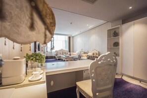 Une cuisine moderne dotée d’un îlot central, un coin repas avec une table et des chaises blanches, et une vue sur un salon avec des canapés.