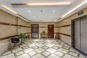 Un hall d’hôtel avec un sol en marbre, un comptoir d’accueil, un fauteuil noir et une porte.