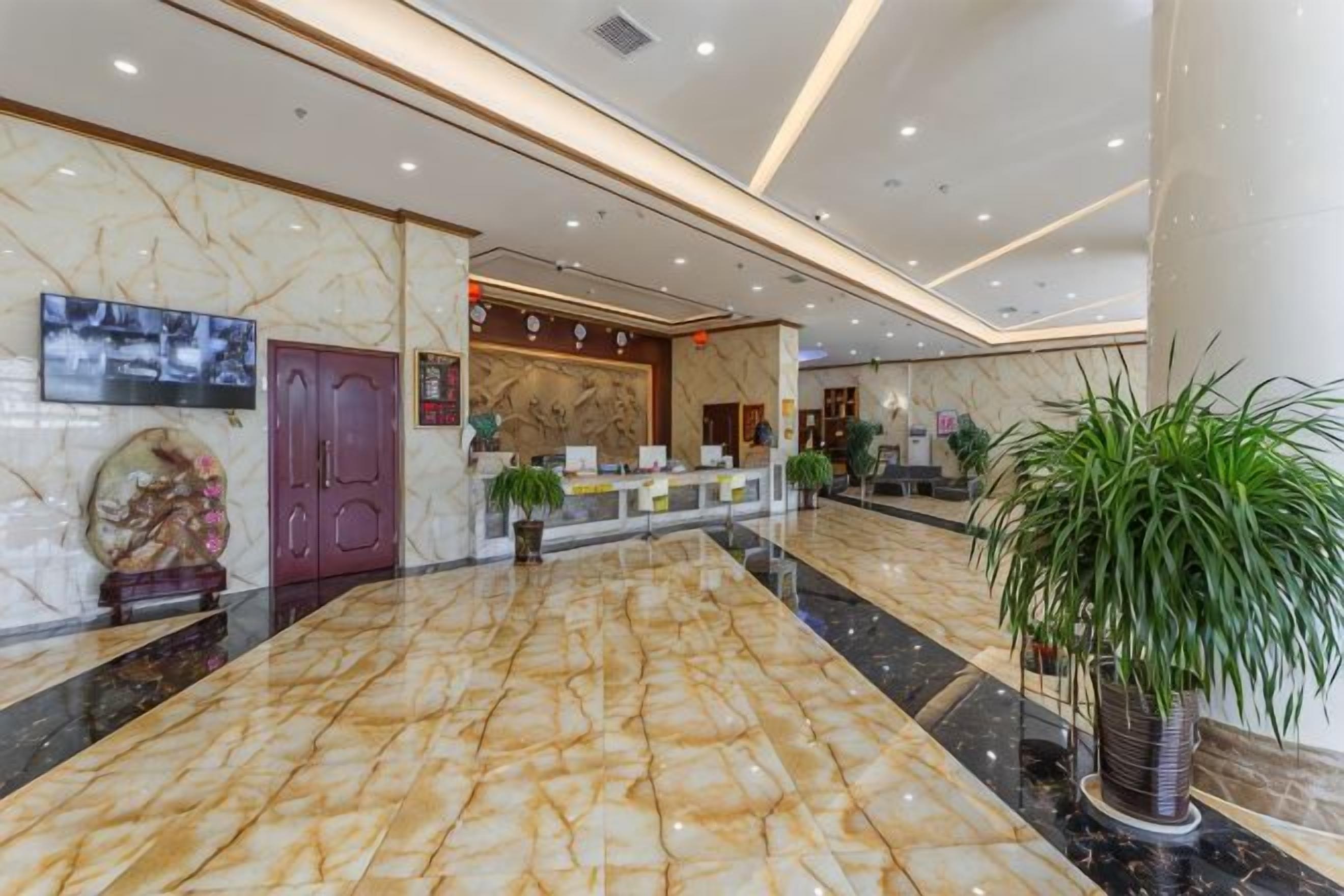 Een hotellobby met marmeren vloeren, een receptiebalie en een grote potplant.