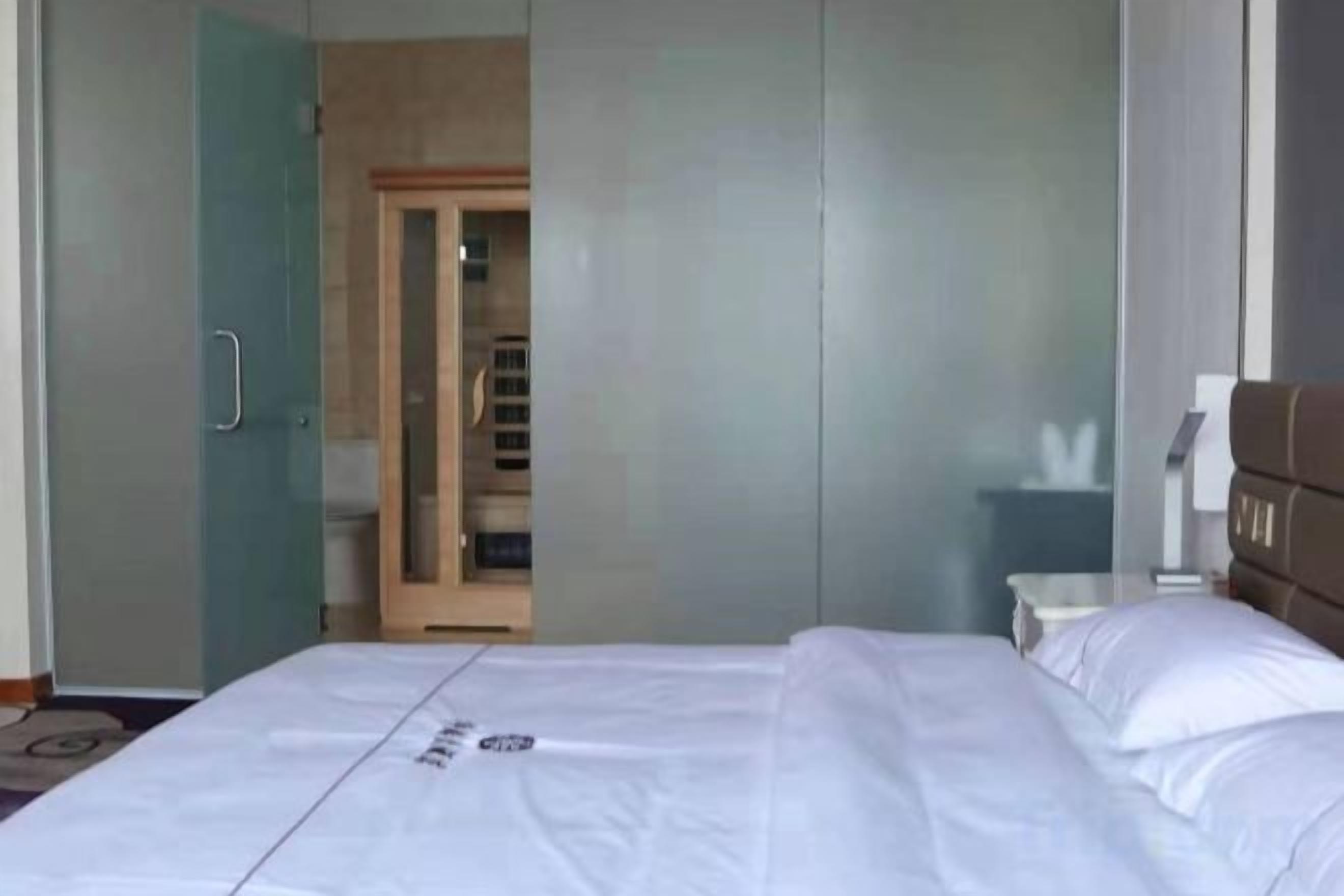 A hotel room with a bed, a wardrobe, and a bathroom visible through a glass door.