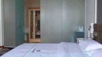 A hotel room with a bed, a wardrobe, and a bathroom visible through a glass door.