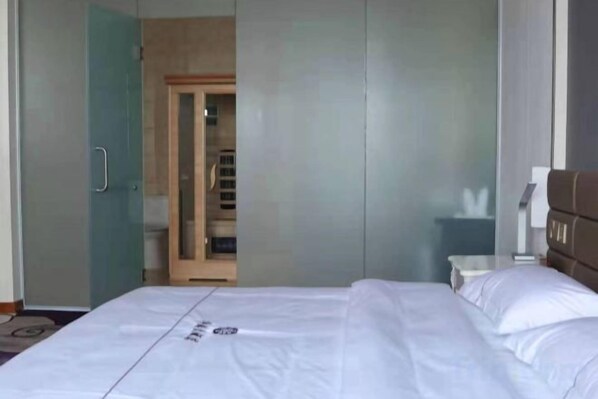 Habitación de hotel con una cama, un armario y un baño visible a través de una puerta de cristal.