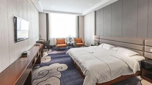 Een hotelkamer met een groot bed, een bureau met stoel, een televisie en een raam met uitzicht.