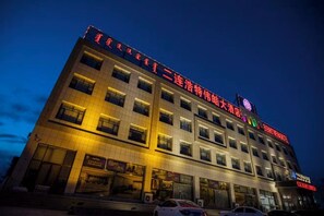 Een meerlaags hotel met verlichte reclameborden, een parkeerplaats en een heldere lucht.