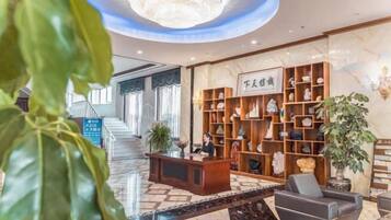 A hotel lobby with a reception desk, a staircase, and a large plant.