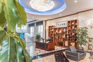 Vestíbulo de hotel con mostrador de recepción, escalera y una planta grande.