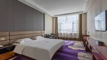 A hotel room with a large bed, a desk with a chair, a TV, and a window with curtains.
