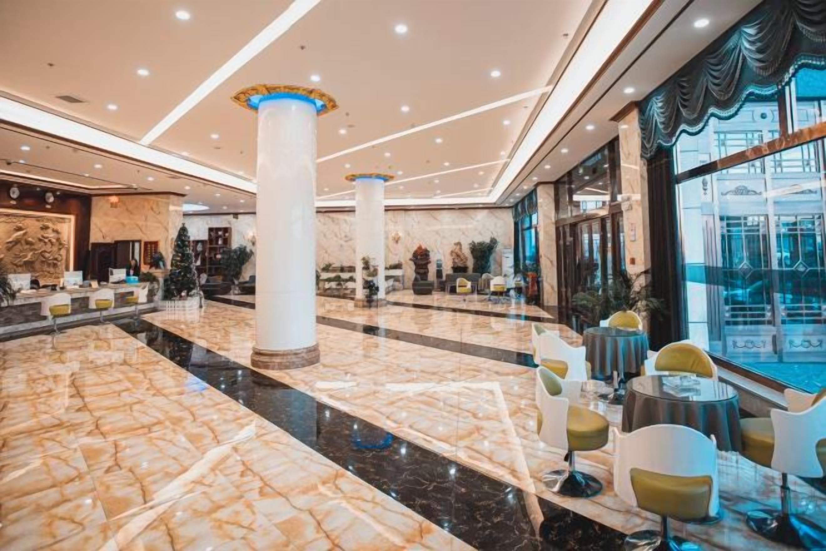A spacious lobby with marble flooring, large columns, and round tables with chairs.