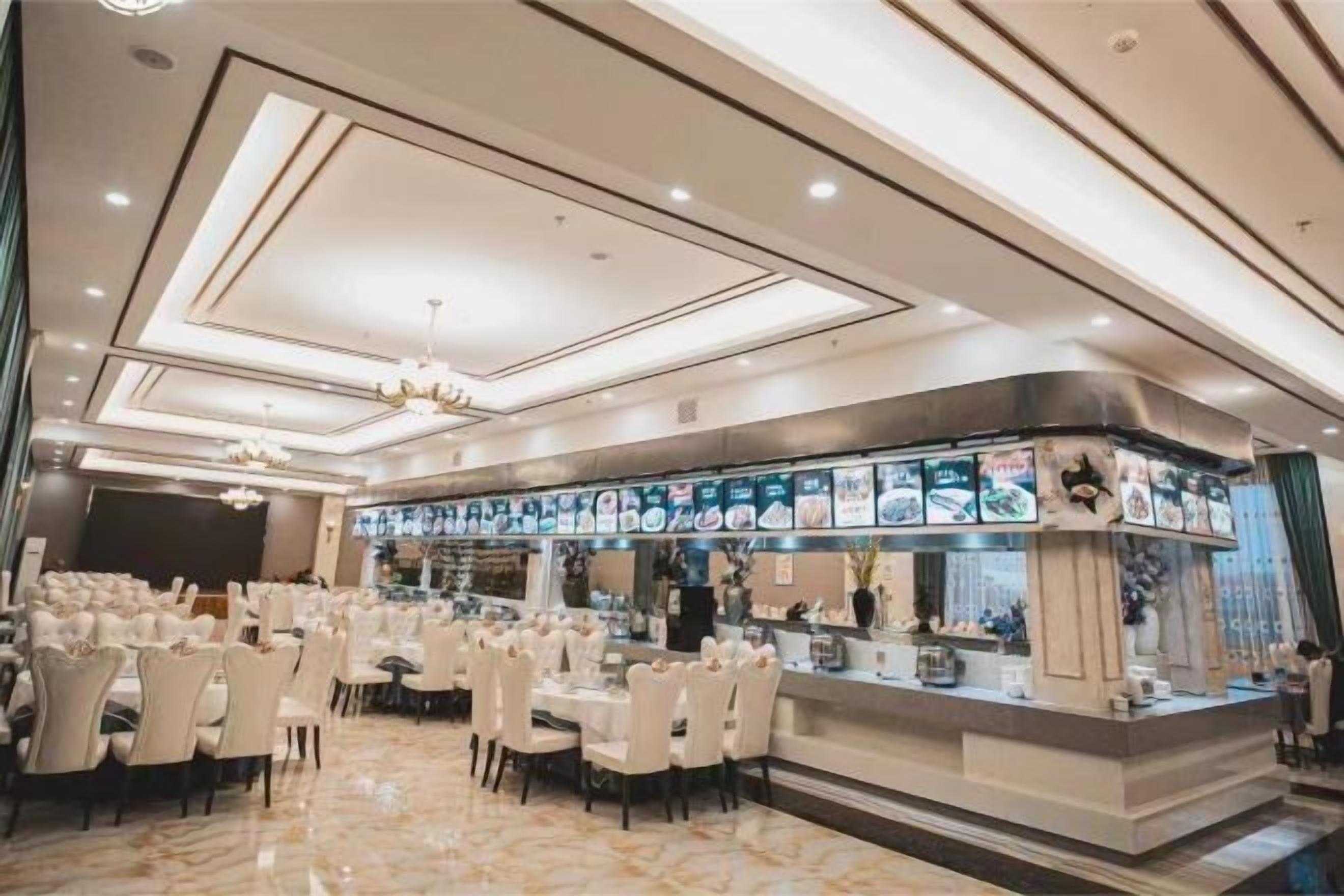 A restaurant with a long counter, multiple tables, and a chandelier.