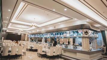 A restaurant with a long counter, multiple tables, and a chandelier.