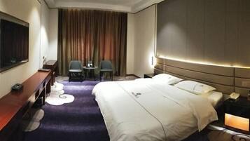 Habitación de hotel con una cama grande, un escritorio, dos sillas, un televisor y una cortina.