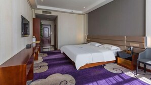 Une chambre d’hôtel avec un grand lit, un bureau et une chaise. Un couloir mène à une autre pièce.