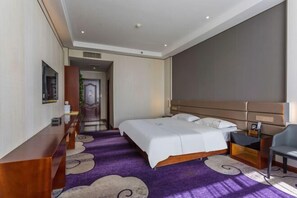 Une chambre d’hôtel avec un grand lit, un bureau et une chaise. Un couloir mène à une autre pièce.