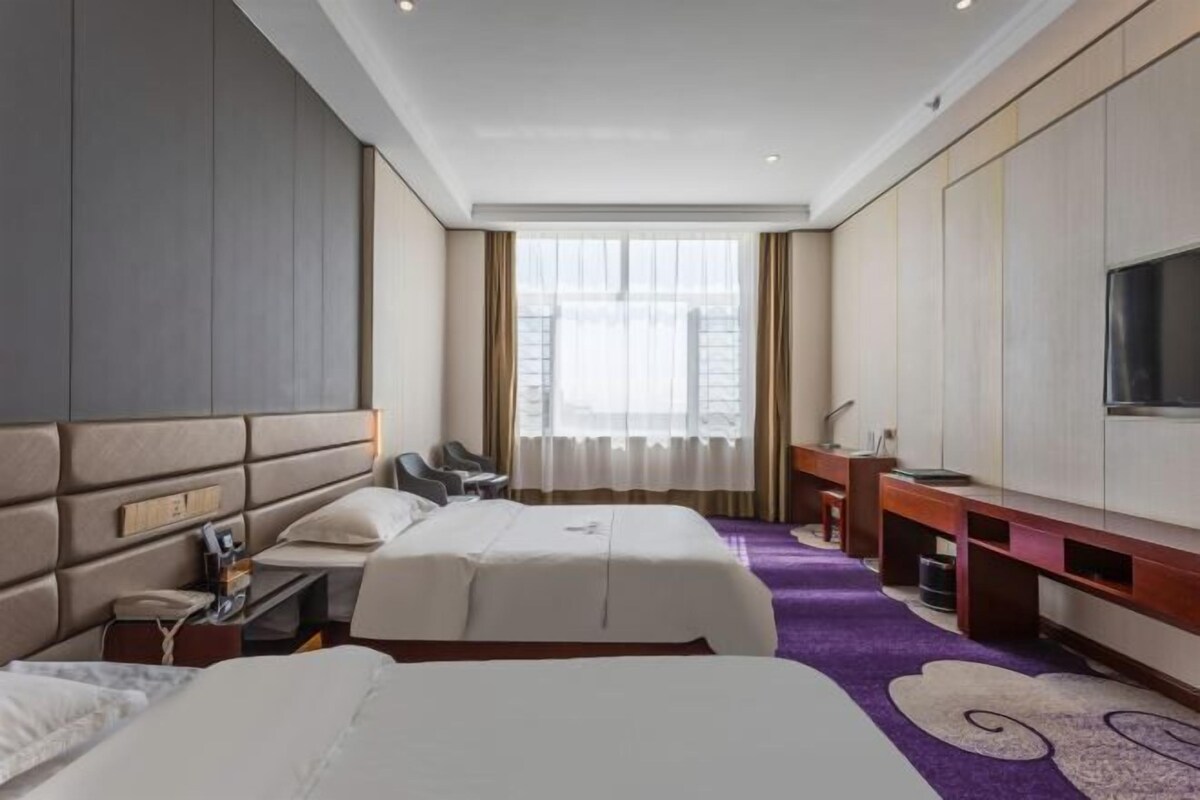 A hotel room with two beds, a desk, a chair, a TV, and a large window.