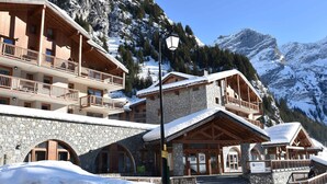 A multi-story wooden building with balconies, stone walls, and a sign indicating it's a ski resort. - Beautiful apartment with balcony and covered parking (Pralognan-la-Vanoise)