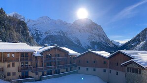 A snow-covered lodge with a wooden exterior and a balcony, set against a backdrop of snow-capped mountains and a clear sky. - Beautiful apartment with balcony and covered parking (Pralognan-la-Vanoise)