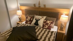 A neatly made bed with a brown and white striped blanket, two nightstands with lamps, and a headboard with small decorative items. - Beautiful apartment with balcony and covered parking (Pralognan-la-Vanoise)