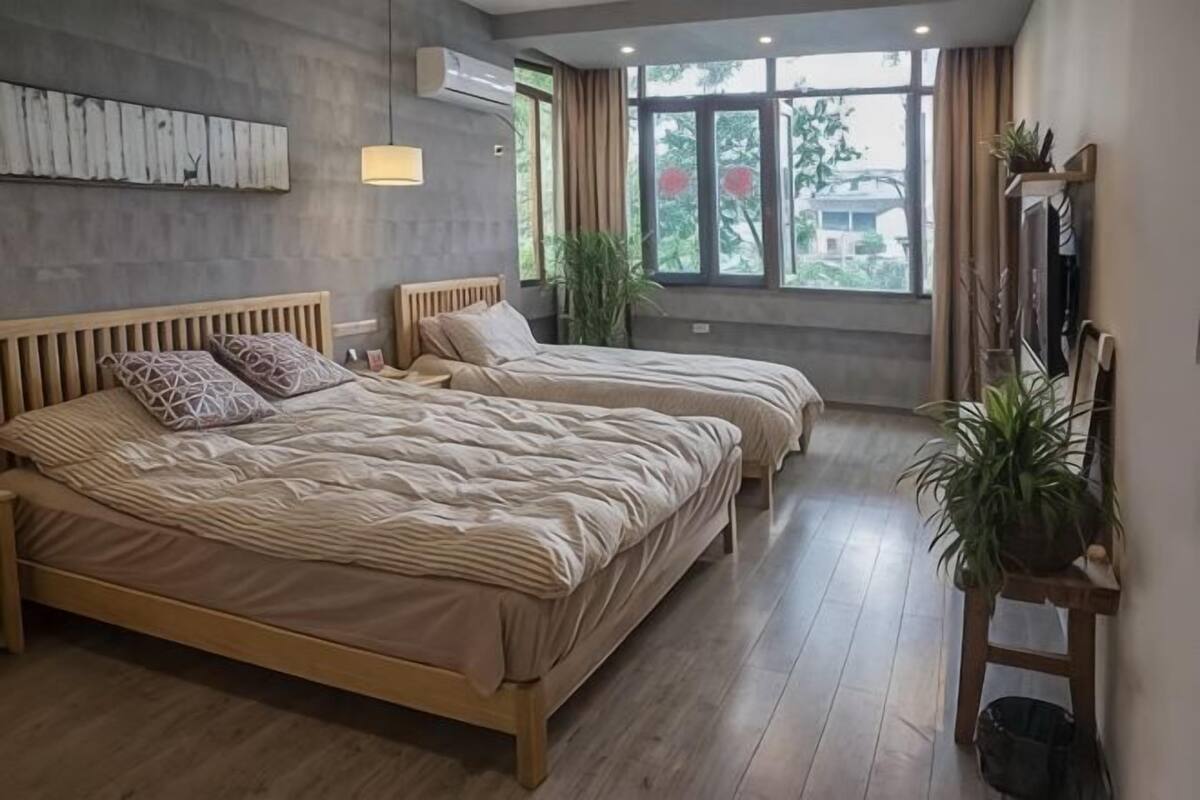 Quarto com duas camas, uma janela grande e uma planta.