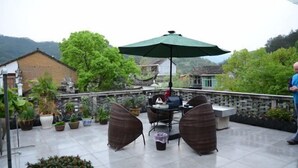 Un patio al aire libre con una mesa y sillas, rodeado de plantas en macetas y un paraguas verde.