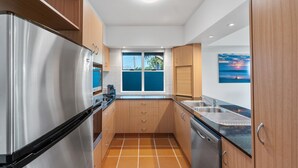 A modern kitchen with stainless steel appliances, wooden cabinets, a window with a view, and a dishwasher. - Riverview Apartment 1 Block 1 (ILUKA)