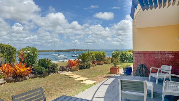A patio with a view of the sea, featuring a bench, chairs, and potted plants. - Riverview Apartment 1 Block 1 (ILUKA)