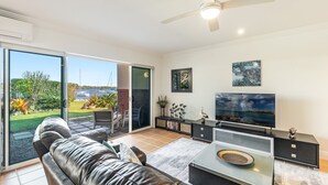 A living room with a sofa, TV, and a view of the sea through a sliding door. - Riverview Apartment 1 Block 1 (ILUKA)