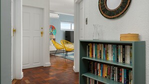 A hallway with a wooden floor, a bookshelf with books, a mirror, and a door leading to another room. - Jagar Court 8 (Cape Town)