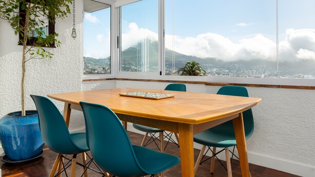 A conference room with a wooden table and teal chairs, large windows with a city and mountain view, and a blue vase with a plant. - Jagar Court 8 (Cape Town)