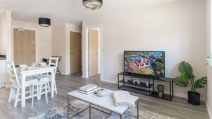 A modern living room with a dining area, a flat-screen TV, and a potted plant.