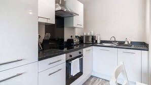 A modern kitchen with white cabinets, a black countertop, a stainless steel range hood, and a built-in oven.