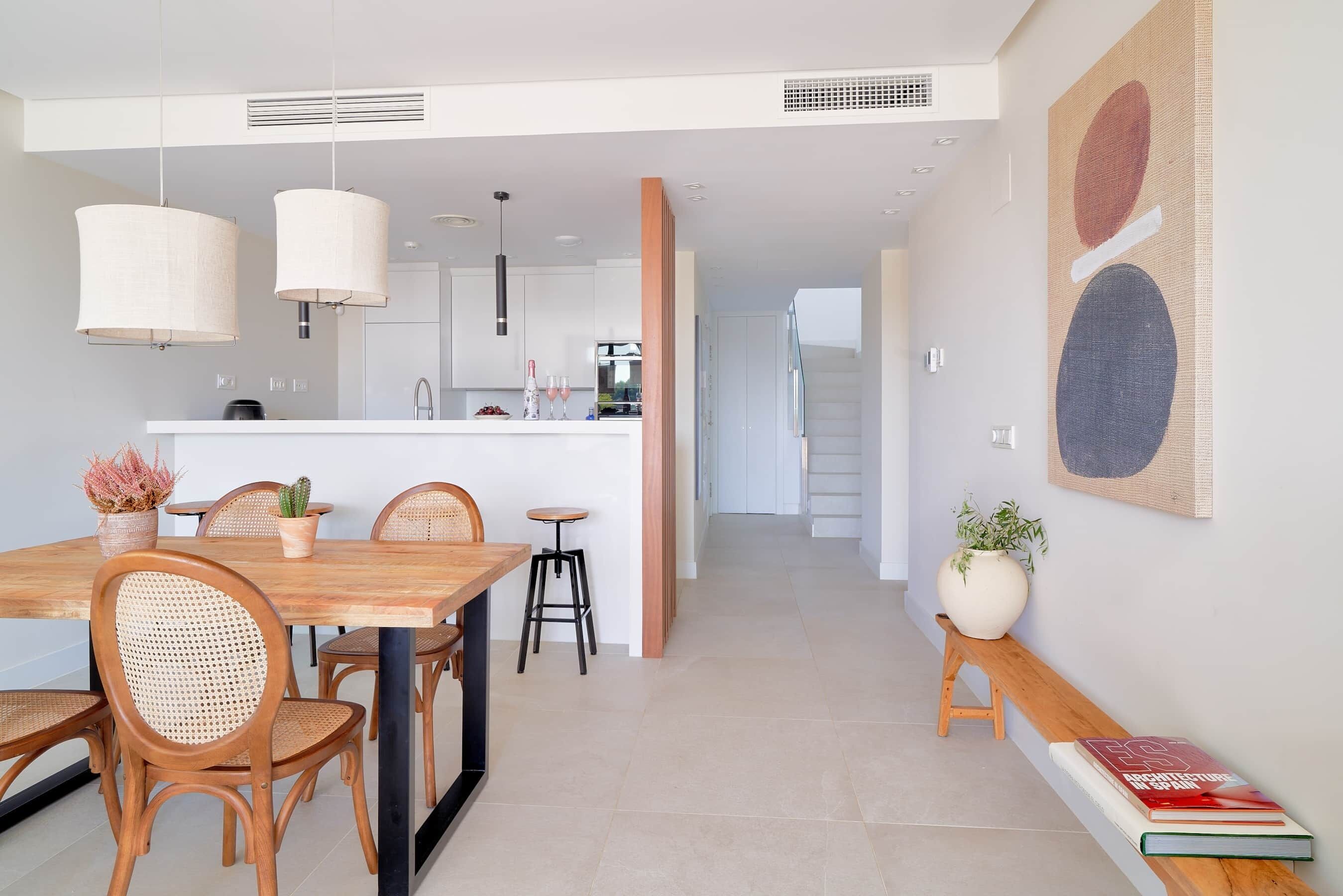 A modern kitchen with white cabinets, a wooden dining table, and pendant lights.