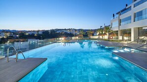 Piscina com água azul cristalina, rodeada por edifícios modernos e vista para uma encosta.