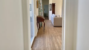 A hallway with wooden flooring, a white sofa, and a wooden side table. - L'orangerie des Ursulines (Bayeux)