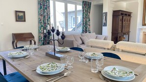A dining area with a wooden table set for a meal, surrounded by sofas and a cabinet. - L'orangerie des Ursulines (Bayeux)