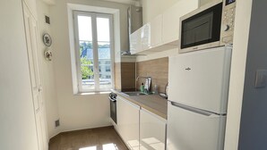A compact kitchen with a window, a microwave, and a refrigerator. - L'orangerie des Ursulines (Bayeux)