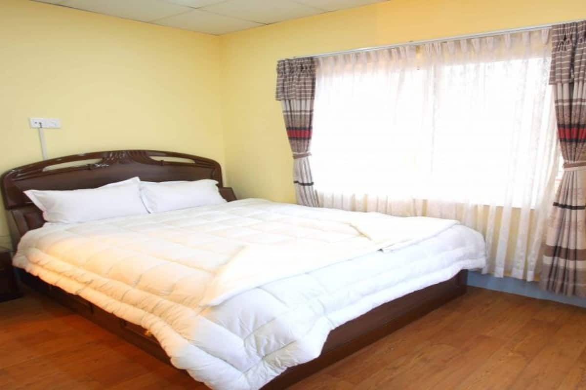 A neatly made bed in a room with a wooden floor and a window with curtains.