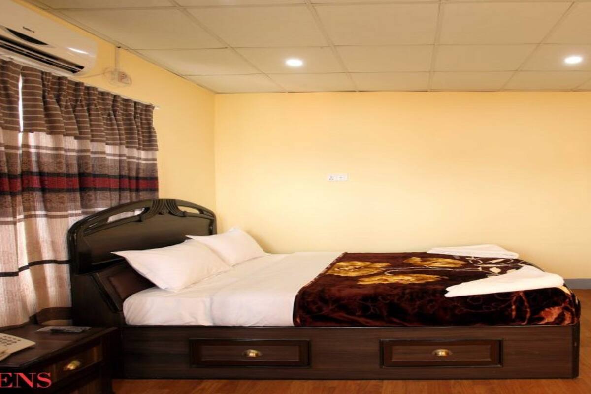 A hotel room with a bed, a nightstand, a wooden floor, and a bathroom visible through an open door.
