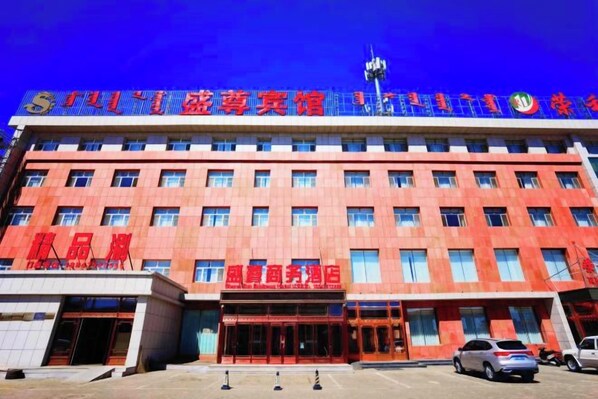 A multi-story building with a red facade, multiple windows, and a prominent entrance. - Shengzun Business Hotel (West Ujimqin Banner)