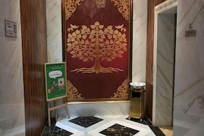 A marble wall with a red and gold decorative panel, a small table with a bowl, and a green sign on an easel. - Shengzun Business Hotel (West Ujimqin Banner)