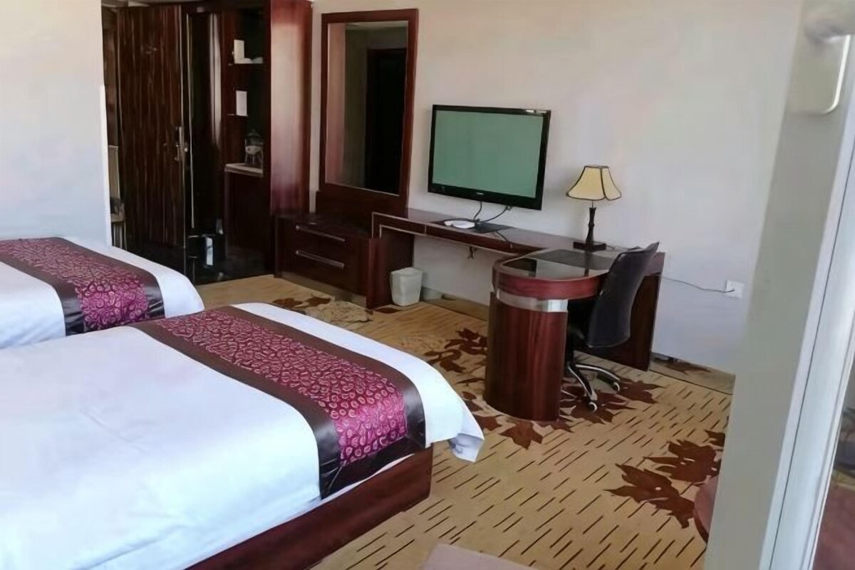 Ein Hotelzimmer mit zwei Betten, einem Schreibtisch, einem Sessel, einem Fernseher und einem Mülleimer.