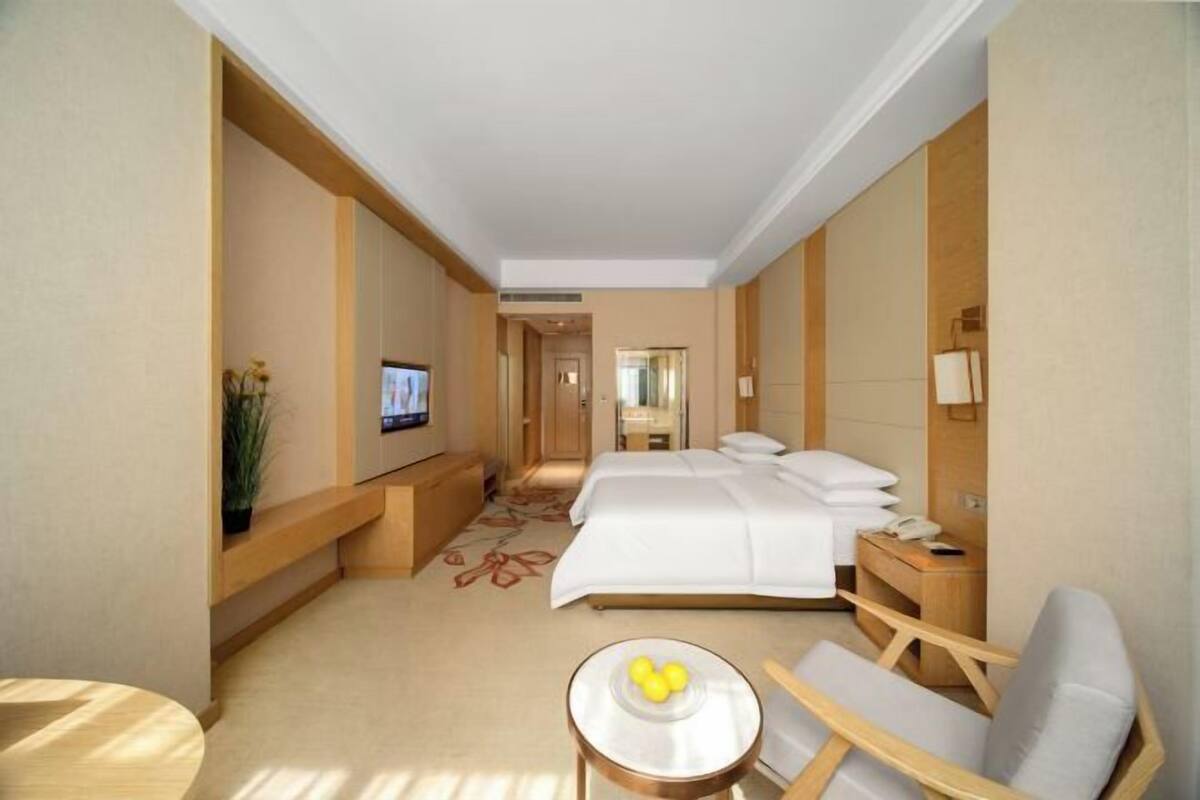 A hotel room with a bed, a TV, a small table with fruit, and a chair.