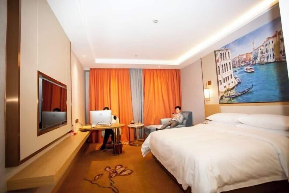 A hotel room with a bed, a desk with a laptop, a chair, and a painting of a canal scene.