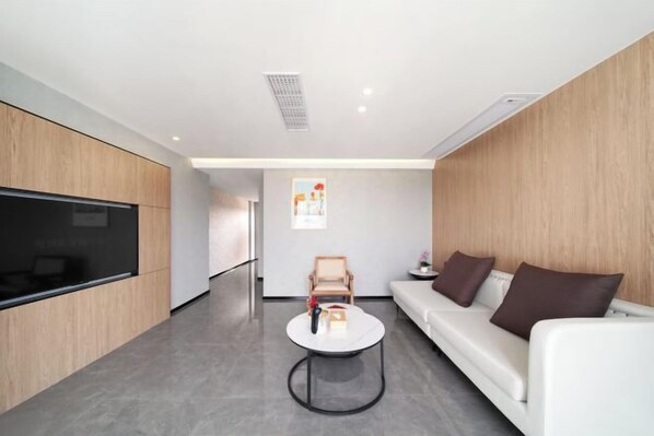 Una sala de estar moderna con un televisor de pantalla plana, un sofá blanco, una mesa de centro y una pared de acento de madera.