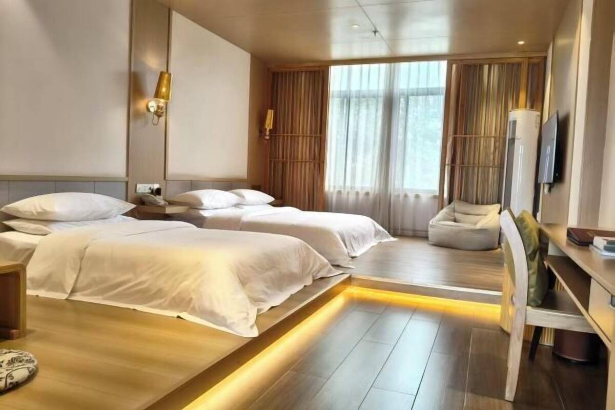 A hotel room with two beds, a desk, a chair, a TV, and a large window with curtains.