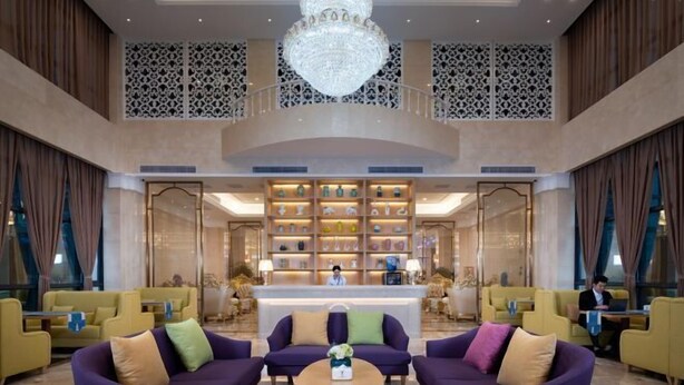 A lobby with a reception desk, purple sofas, and a chandelier. - Venus Resort (Yidu)