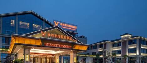A modern hotel with a prominent entrance, signage for a restaurant, and a well-lit facade.